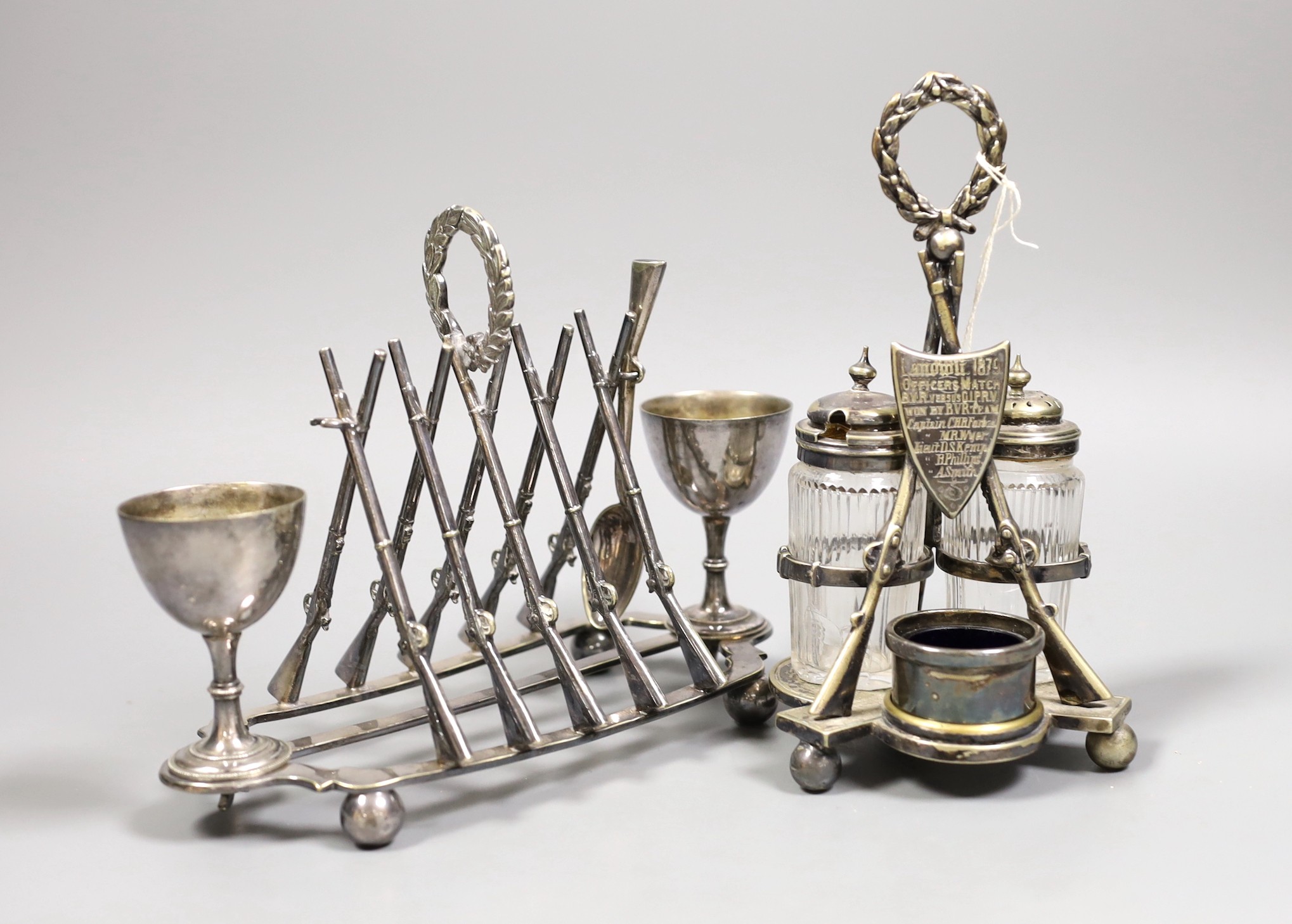 Two plated rifle trophies: toastrack and cruet set, tallest 20cm